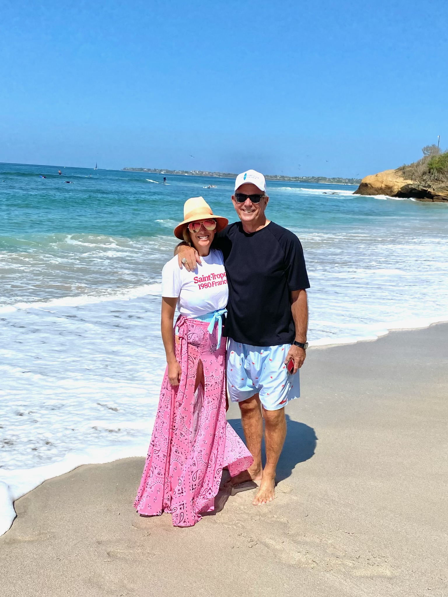Mac and Laura standing arm in arm on the beach with the ocean behind them