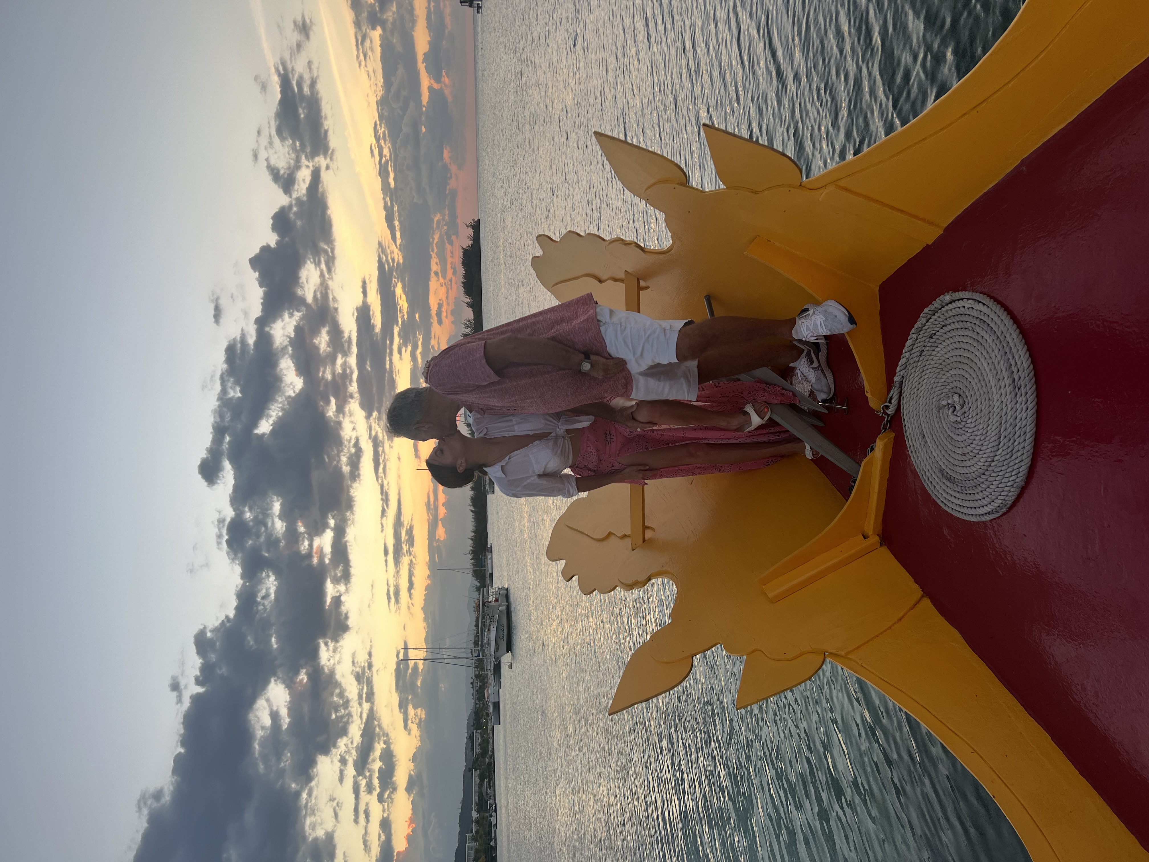 Mac and Laura kissing on the bow of a boat at sunset